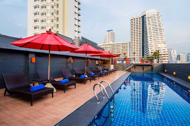 The rooftop pool in daylight, loungers and red parasols along the deck