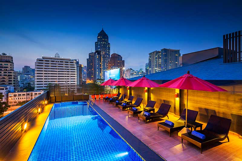 The rooftop pool lit at night, with the towers of Sukhumvit beyond the railing